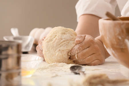 Female chef preparing dough on kitchen table, closeup