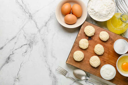Wooden board with raw lazy dumplings and ingredients on light backgroundの写真素材
