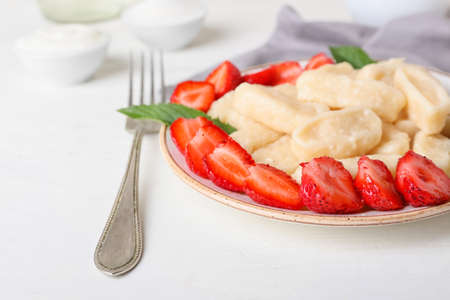 Plate with delicious lazy dumplings, ripe strawberry and fork on light wooden background, closeupの写真素材