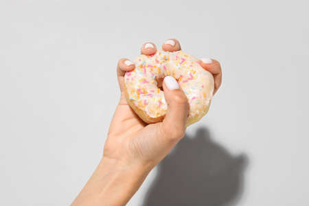 Woman with beautiful manicure squeezing donut on light backgroundの写真素材