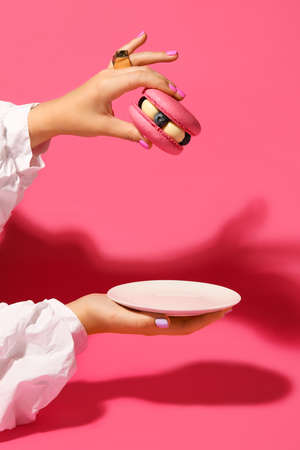 Elegant woman with beautiful manicure and trendy jewelry holding saucer and macaron on color backgroundの写真素材