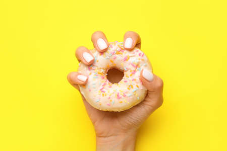 Woman with beautiful manicure holding delicious donut on yellow backgroundの写真素材