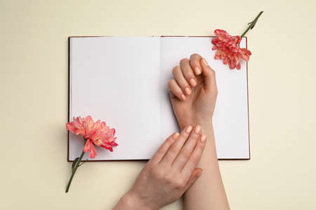 Hands with beautiful manicure, flowers and book on light backgroundの写真素材