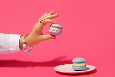 Elegant woman with beautiful manicure and stylish jewelry holding macaron on color backgroundの写真素材