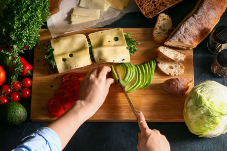 Woman preparing tasty sandwiches on dark background