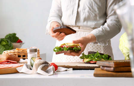 Woman preparing tasty sandwiches on light background