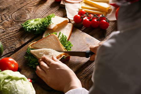 Woman cutting tasty sandwich on wooden background