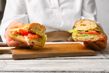 Woman holding tasty sandwiches on light wooden background