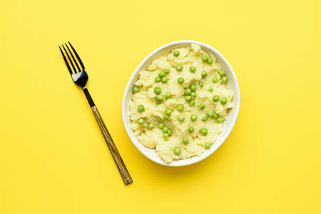 Bowl of mashed potatoes with green peas and fork on color backgroundの写真素材