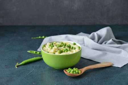 Bowl with mashed potatoes, green peas and spoon on color backgroundの写真素材