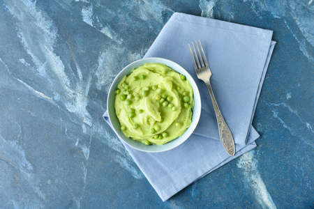 Bowl with mashed potatoes, green peas and fork on color backgroundの写真素材
