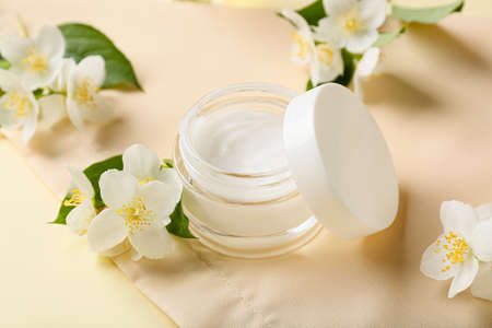 Jar of cream and jasmine flowers on color background