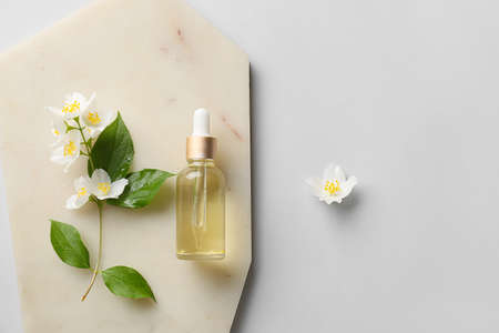 Board with bottle of essential oil and jasmine flowers on gray backgroundの写真素材