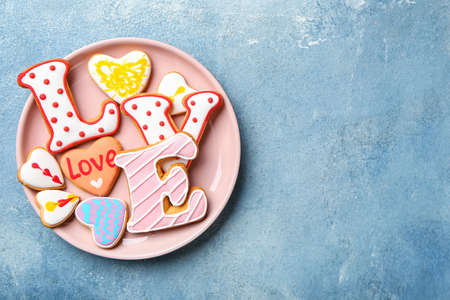 Plate with word LOVE made of cookies on blue background