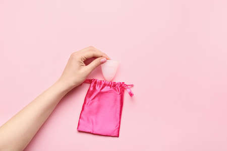 Female hand with menstrual cup and bag on color backgroundの写真素材