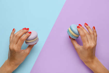 Woman with beautiful manicure holding delicious macaroons on color backgroundの写真素材