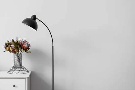 Vase with flowers on shelf and black standing lamp near light wallの写真素材