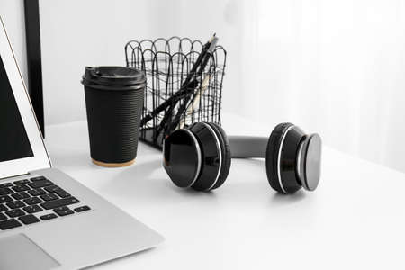 Black headphones and cup of coffee on table in light roomの写真素材