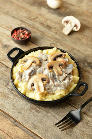 Frying pan with tasty mashed potatoes, mushrooms and peppercorns on wooden backgroundの写真素材