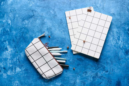 Pencil case with stationery supplies and notebooks on color background