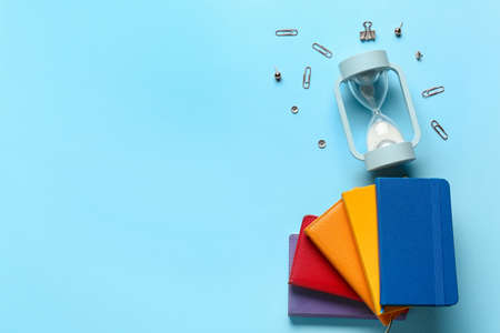 Notebooks and hourglasses on color background