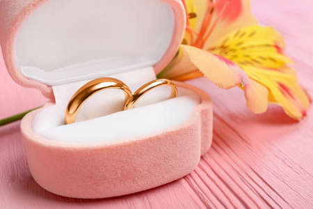 Box with wedding rings and alstroemeria flower on color wooden tableの写真素材