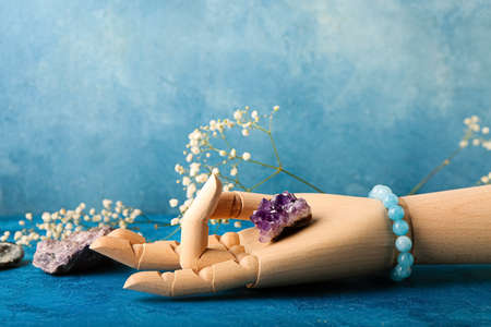 Wooden hand making mudra, gemstones and flowers on color backgroundの写真素材