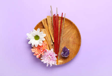 Plate with incense, gemstone, flowers and Palo Santo on color background