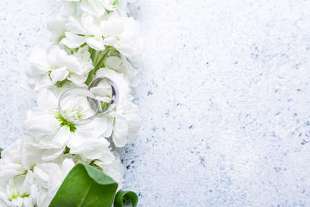 Wedding rings and beautiful flowers on light tableの写真素材