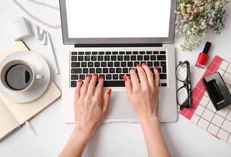 Woman with beautiful manicure working with laptop on white table