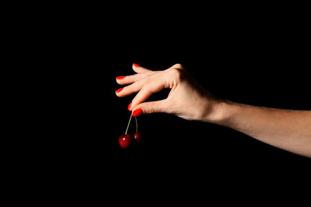 Woman with beautiful manicure holding cherry on dark background