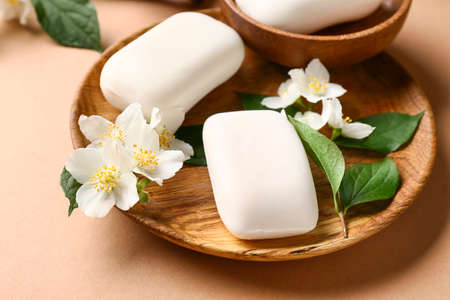 Plate with soap bars and flowers on color background, closeup