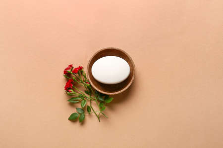 Bowl with soap bar and flowers on color background