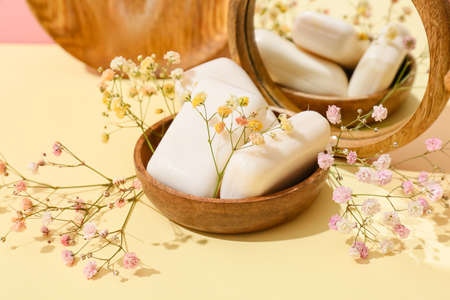Bowl with soap bars, flowers and mirror on color background