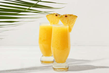 Glasses of tasty pineapple smoothie and tropical leaf on light backgroundの写真素材
