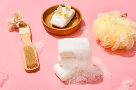 Stack of soap bars with foam and bath supplies on color background