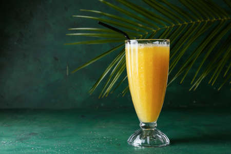 Glass of tasty pineapple smoothie and tropical leaf on color background
