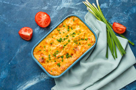 Casserole with mashed potatoes and tomato on color background