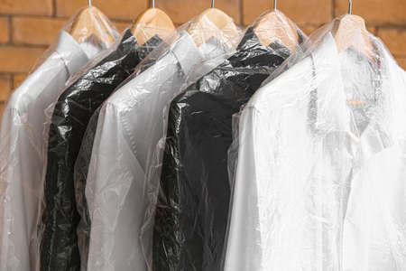 Rack with clean shirts in plastic bags near brick wallの写真素材