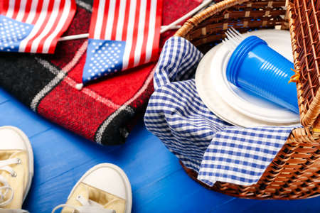 Picnic basket with American flags, plaid and shoes on color wooden backgroundの写真素材