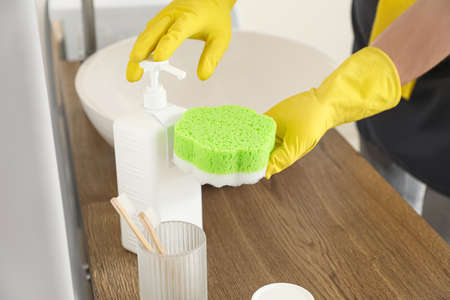 Young man pouring detergent onto sponge in bathroom, closeup