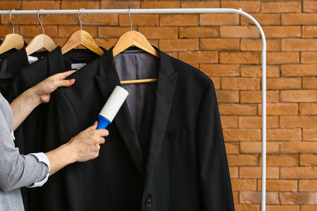 Woman cleaning jacket with lint roller near brick wall