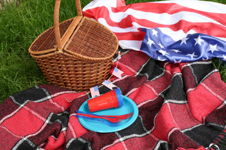 Dinnerware with picnic basket and American flag on plaid in parkの写真素材