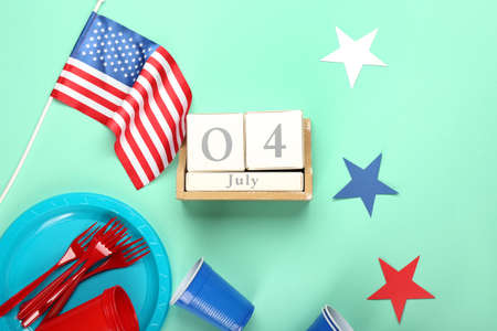 Calendar with date of Independence Day, American flag and tableware on color background