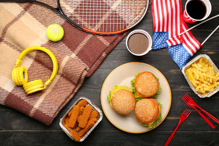 American flags with traditional food, plaid, headphones and tennis racket on dark wooden background