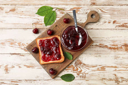 Bowl and toast with cherry jam on wooden background