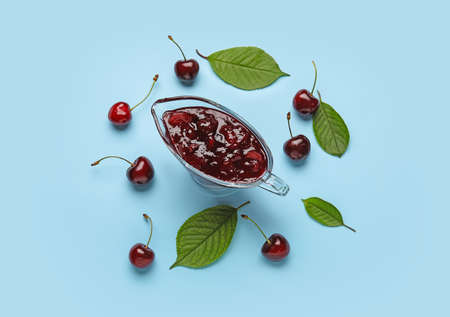 Gravy boat of tasty cherry jam on color backgroundの写真素材