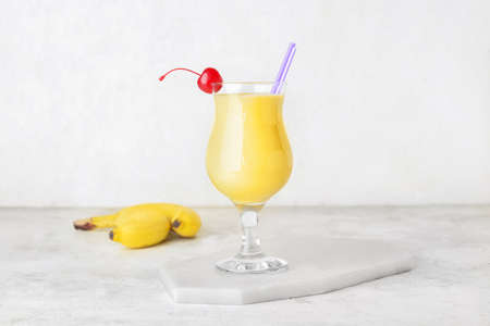 Glass of tasty banana daiquiri cocktail and fruits on light backgroundの写真素材