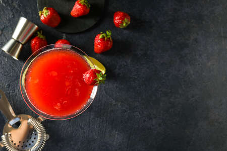 Glass of strawberry daiquiri cocktail and berries on dark background