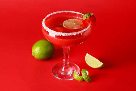 Glass of strawberry daiquiri cocktail and limes on color backgroundの写真素材